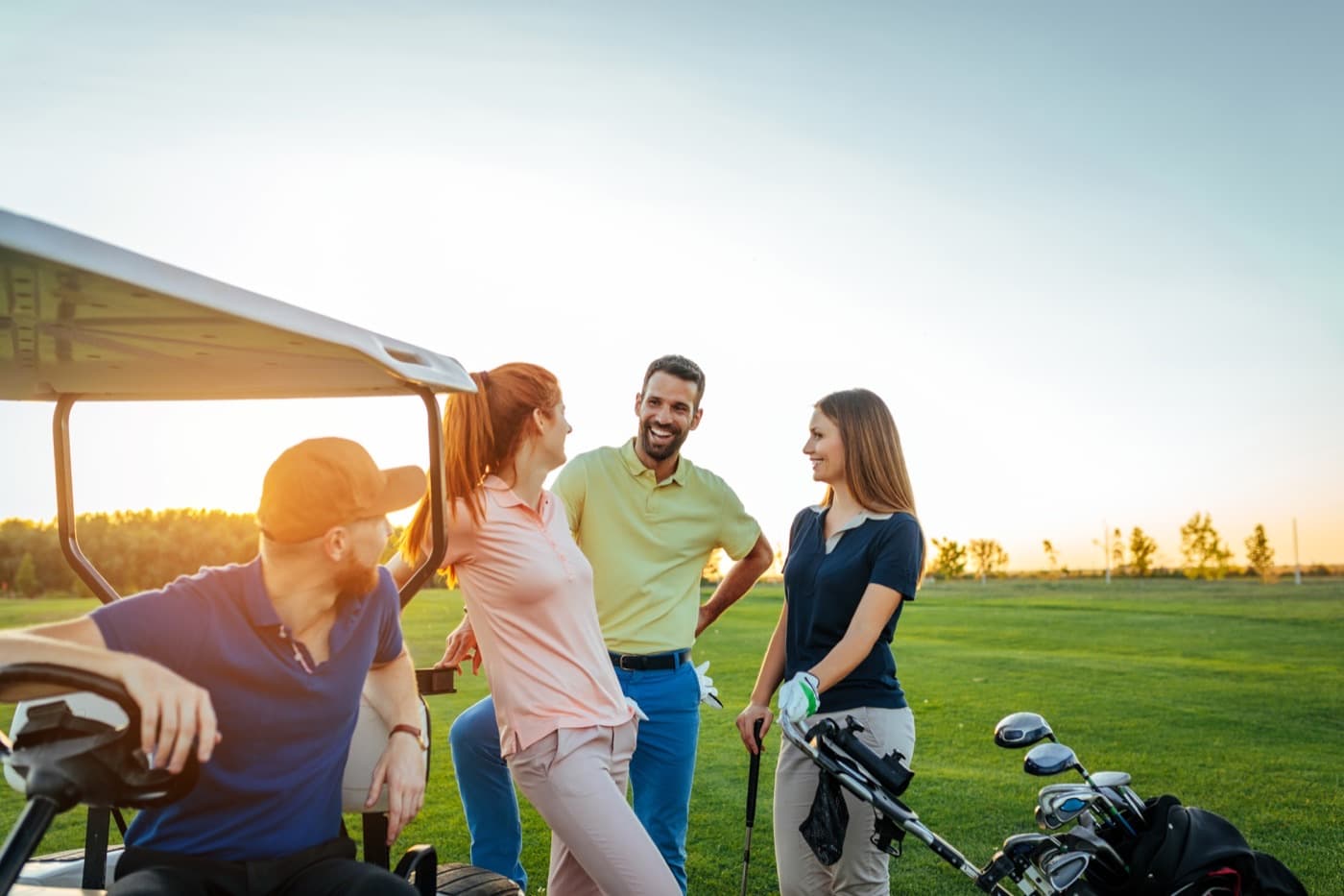Four golfers talking by a cart at sunset